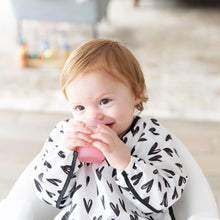 Load image into Gallery viewer, A toddler uses a Bumkins Silicone Starter Cup: Pink while in a high chair, wearing a white bib with black hearts.
