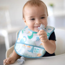 Load image into Gallery viewer, A baby in Bumkins Starter Bib 2 Pack: Dinosaurs &amp; Blue Tropic holds a gray baby fork in a high chair.
