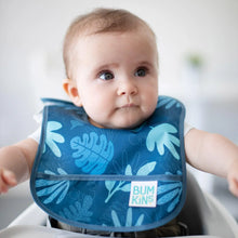 Load image into Gallery viewer, A baby in a blue Bumkins Starter Bib 2 Pack: Dinosaurs &amp; Blue Tropic looks off to the side.
