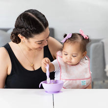 Load image into Gallery viewer, A woman smiles as baby, in a pink Bumkins Starter Bib 2 Pack: Floral &amp; Lace, reaches for a purple bowl on a white table.

