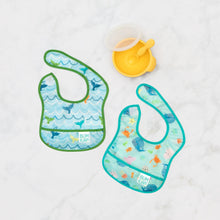 Load image into Gallery viewer, Bumkins Starter Bib 2 Pack: Ocean Life &amp; Whale Tail lays flat on a marble background next to a yellow bowl &amp; spoon set.
