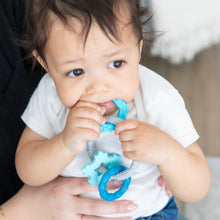 Load image into Gallery viewer, Close-up of a child chewing a Bumkins Silicone Teething Charms: Blue while being held by adult hands.
