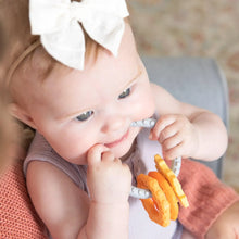 Load image into Gallery viewer, A baby in a purple outfit, wearing a white bow, enjoys teething relief with Bumkins Silicone Teething Charms: Orange on someone's lap.
