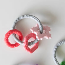 Load image into Gallery viewer, Bumkins Silicone Teething Charms: Pink rests on a white background with another teething toy nearby.
