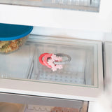 Close-up of a glass refrigerator shelf with a Bumkins Silicone Teething Charms: Pink  beside a covered bowl of food.