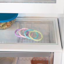 Load image into Gallery viewer, Bumkins Silicone Teething Rings 4 Pack: Spring sits beside a blue-lidded bowl on a glass refrigerator shelf.
