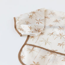 Load image into Gallery viewer, Close-up of Bumkins Sleeved Bib: Palm Daze on a white background, with focus on the white elastic cuff on the sleeve.
