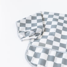 Load image into Gallery viewer, Close-up of Bumkins Sleeved Bib: Charcoal Check on a white background, with focus on the white elastic cuff on the sleeve.
