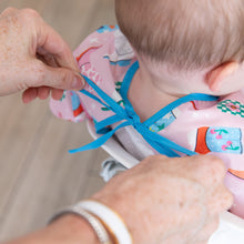 Load image into Gallery viewer, Adult hands tie the ribbon closure on Bumkins Sleeved Bib: Boots, worn by a baby in a high chair.
