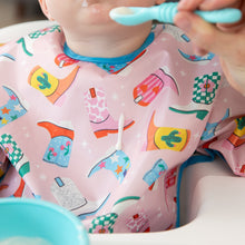 Load image into Gallery viewer, A baby enjoys feeding time while wearing Bumkins Sleeved Bib: Boots, while a drop of yogurt falls down the front of the bib.
