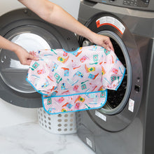 Load image into Gallery viewer, A person holds Bumkins Sleeved Bib: Boots in front of an open front-loading washer, with a laundry basket nearby.

