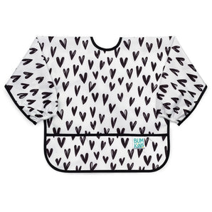 Bumkins Sleeved Bib: Hearts is a white waterproof bib with a black heart pattern, black trim, front pocket, and long sleeves.