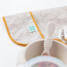 Load image into Gallery viewer, Close-up of a folded Bumkins Sleeved Bib: Wander on a white background, with a blurred bowl and spoon in the foreground.
