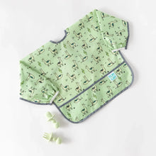 Load image into Gallery viewer, Bumkins Sleeved Bib: Llamas rests on a white background with light green silicone utensils nearby.
