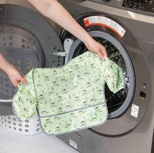 Load image into Gallery viewer, A person holds Bumkins Sleeved Bib: Llamas in front of an open front-loading washing machine.

