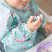 Load image into Gallery viewer, Close-up of a toddler covered in yogurt, wearing a Bumkins Sleeved Bib: Rainbows.
