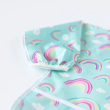Load image into Gallery viewer, Close-up of Bumkins Sleeved Bib: Rainbows on a white background, with focus on the white elastic cuff on the sleeve.
