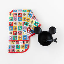 Load image into Gallery viewer, Bumkins Sleeved Bib: Mickey &amp; Friends Check Mates is shown folded on a white background next to a black Mickey-shaped bowl with spoon.
