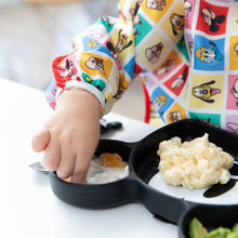 Load image into Gallery viewer, A child in Bumkins Sleeved Bib: Mickey &amp; Friends Check Mates enjoys baby-led weaning from a divided plate with macaroni at the table.
