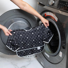 Load image into Gallery viewer, A person holds Bumkins Sleeved Bib: Mickey Mouse Icon Black + White in front of an open front-loading washing machine.
