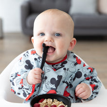 Load image into Gallery viewer, A baby in a high chair wearing a blue bib eats oatmeal and berries from a Bumkins Silicone First Feeding Set: Mickey Mouse Classic Black.
