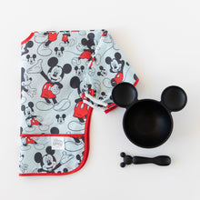 Load image into Gallery viewer, Bumkins Sleeved Bib: Mickey Mouse lays folded next to a black Mickey Mouse-shaped bowl and matching spoon on a white background.
