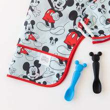 Load image into Gallery viewer, Close-up of Bumkins Sleeved Bib: Mickey Mouse folded on a white background next to 2 spoons with Mickey-shaped handles on a white background.
