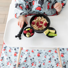 Load image into Gallery viewer, A baby in a high chair wearing a blue bib eats oatmeal &amp; fruit from Bumkins Silicone First Feeding Set: Mickey Mouse Classic Black.
