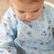 Load image into Gallery viewer, A child wearing a Bumkins Sleeved Bib: Mickey + Minnie Sunny Side Up looks down with a serious expression.
