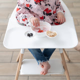 A young girl wearing a Bumkins Sleeved Bib: Minnie Mouse in a highchair eating from the Silicone First Feeding Set: Vanilla Sprinkle.
