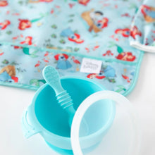 Load image into Gallery viewer, Close-up of a blue baby bowl and spoon on a white background, with Bumkins Sleeved Bib: Ariel blurred behind.
