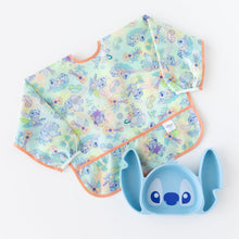 Load image into Gallery viewer, Bumkins Sleeved Bib: Aloha Stitch lays next to a Stitch-shaped silicone plate on a white background.
