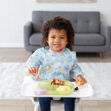 Load image into Gallery viewer, A toddler with curly hair smiles in a high chair, enjoying breakfast on a green plate, wearing a Bumkins Sleeved Bib: Aloha Stitch.
