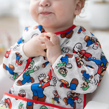 Load image into Gallery viewer, Close-up of a child in a high chair wearing a Bumkins Sleeved Bib: Super Mario™ Classic.
