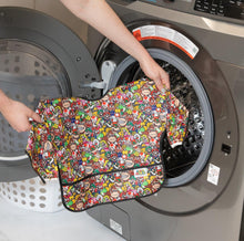 Load image into Gallery viewer, A person holds Bumkins Sleeved Bib: Super Mario™ Mashup in front of an open front-loading washing machine.

