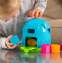 Load image into Gallery viewer, Child engages problem-solving skills with Fat Brain Toy Cos Shape Factory, fitting a blue block into the colorful dome.
