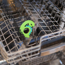 Load image into Gallery viewer, Bumkins Silicone Teether: Dinosaur sits in the top rack of an open dishwasher.
