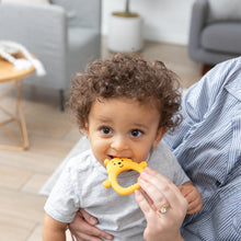 Load image into Gallery viewer, A baby with curly hair chews on a Bumkins Silicone Flat Teether: Winnie the Pooh, soothing gums while being held indoors.
