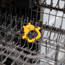 Load image into Gallery viewer, Bumkins Silicone Flat Teether: Winnie the Pooh sits in the top rack of an open dishwasher.
