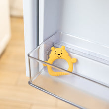 Load image into Gallery viewer, Bumkins Silicone Flat Teether: Winnie the Pooh sits in the side compartment of an open refrigerator door.

