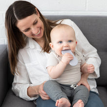 Load image into Gallery viewer, A woman smiles at a baby chewing a Bumkins Silicone Teether: Nintendo SNES™ Controller, with a white brick wall behind them on a gray couch.
