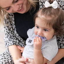 Load image into Gallery viewer, A toddler sits on an adult's lap, happily chewing a Bumkins Silicone Teether: Nintendo SNES™ Controller, while the adult smiles.
