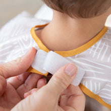 Load image into Gallery viewer, Hands fastening the hook-and-loop closure of a Bumkins Junior Bib: Wander around a child's neck.
