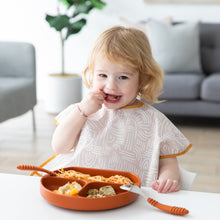 Load image into Gallery viewer, A blonde toddler in a Bumkins Junior Bib: Wander smiles while eating from a divided plate in a brightly lit room.
