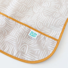 Load image into Gallery viewer, Close-up of Bumkins Junior Bib: Wander on a white background, featuring abstract white lines on beige, with focus on the catch-all pocket.
