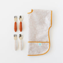 Load image into Gallery viewer, Two sets of baby utensils with orange &amp; beige handles rest next to a folded Bumkins Junior: Bib Wander on a white background.
