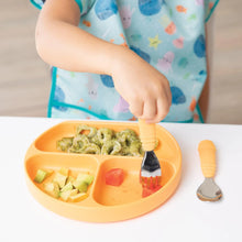 Load image into Gallery viewer, A child in a Bumkins Junior Bib: Ocean Life eating pasta, avocado, and fruit from an orange sectioned plate using an orange fork.
