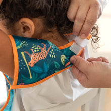 Load image into Gallery viewer, Hands adjusts the hook-and-loop closure of Bumkins Junior Bib: Jungle around a child's neck.
