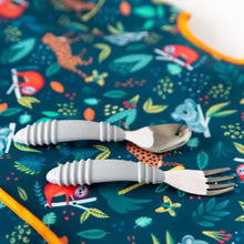 Load image into Gallery viewer, Close-up of a gray spoon and fork resting on a Bumkins Junior Bib: Jungle.
