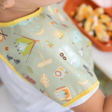 Load image into Gallery viewer, Close-up of a child in a Bumkins Junior Bib: Camp Gear, with focus on the child's shoulder. A plate of food is blurred in the background.
